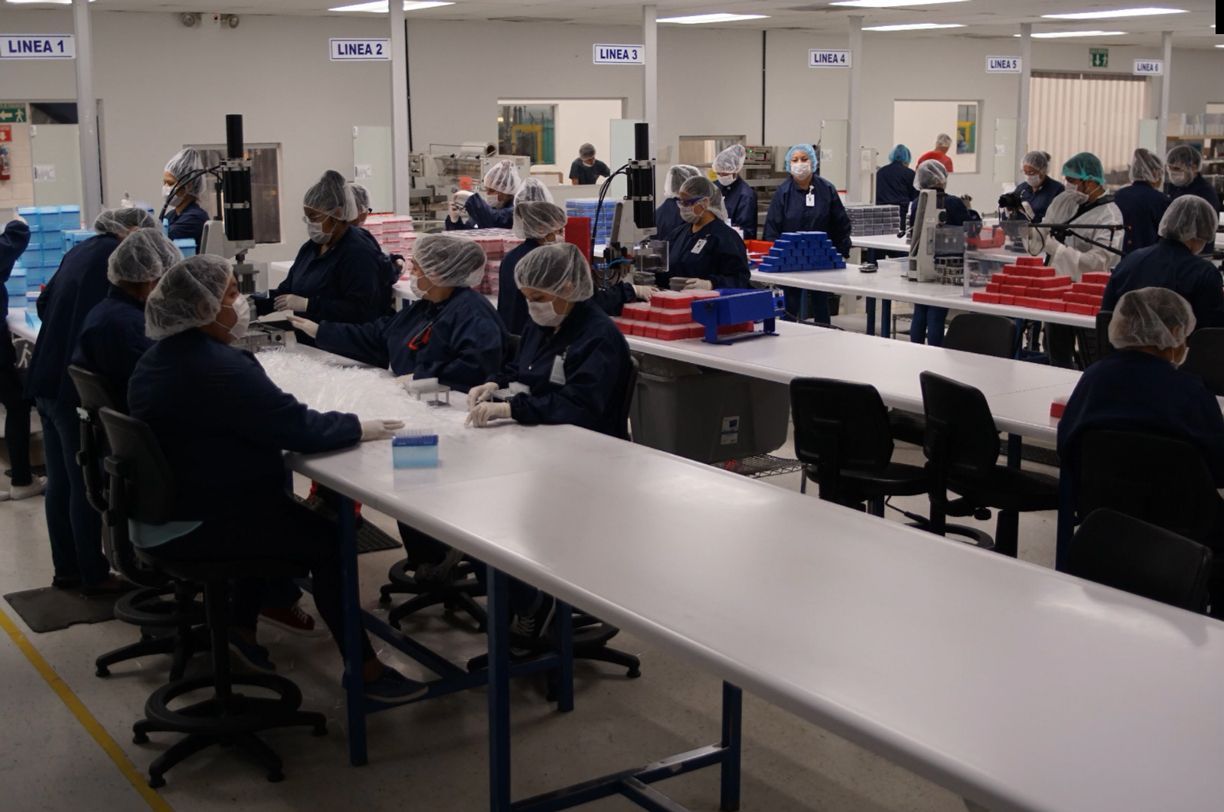 A group of people are sitting at long tables in a factory