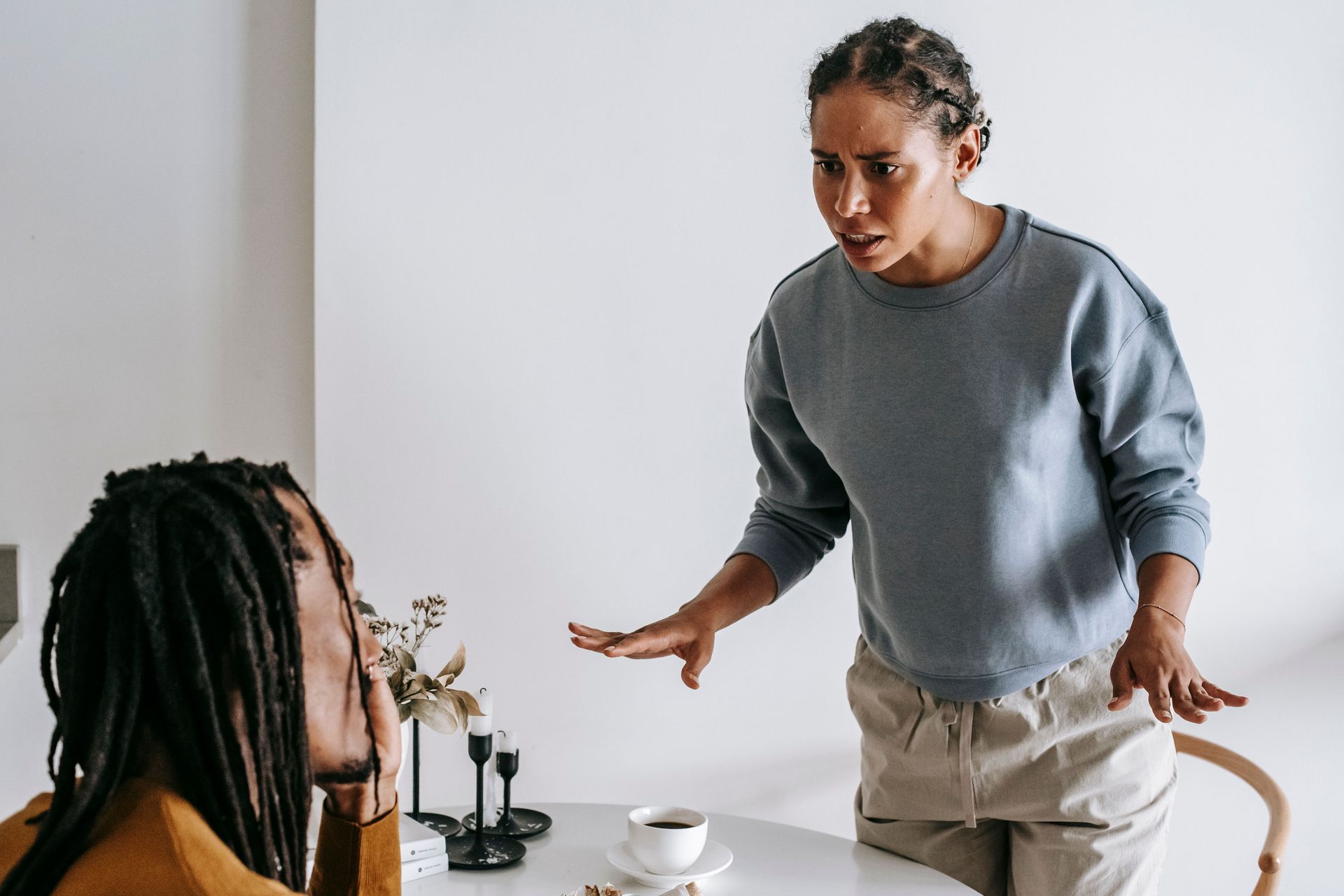 A woman getting frustrated with a man. The man is seated in a chair and she is trying to communicate with him