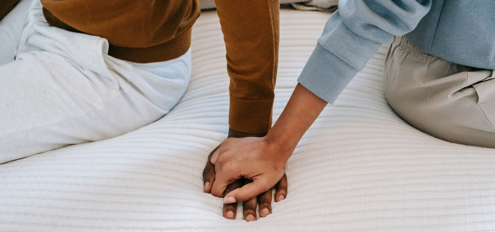 A couple sitting on a bed holding hands, a calm moment of connection in ADHD and relationships