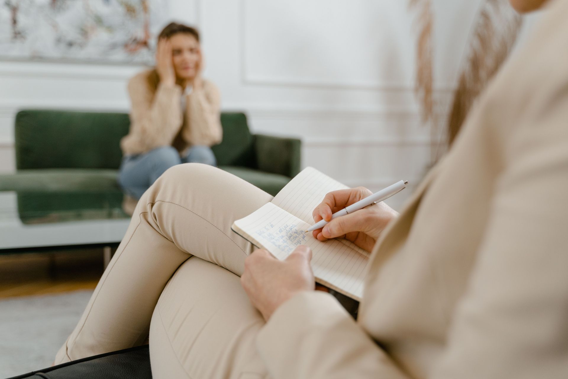 Therapist taking notes during a session while a client sits on a couch