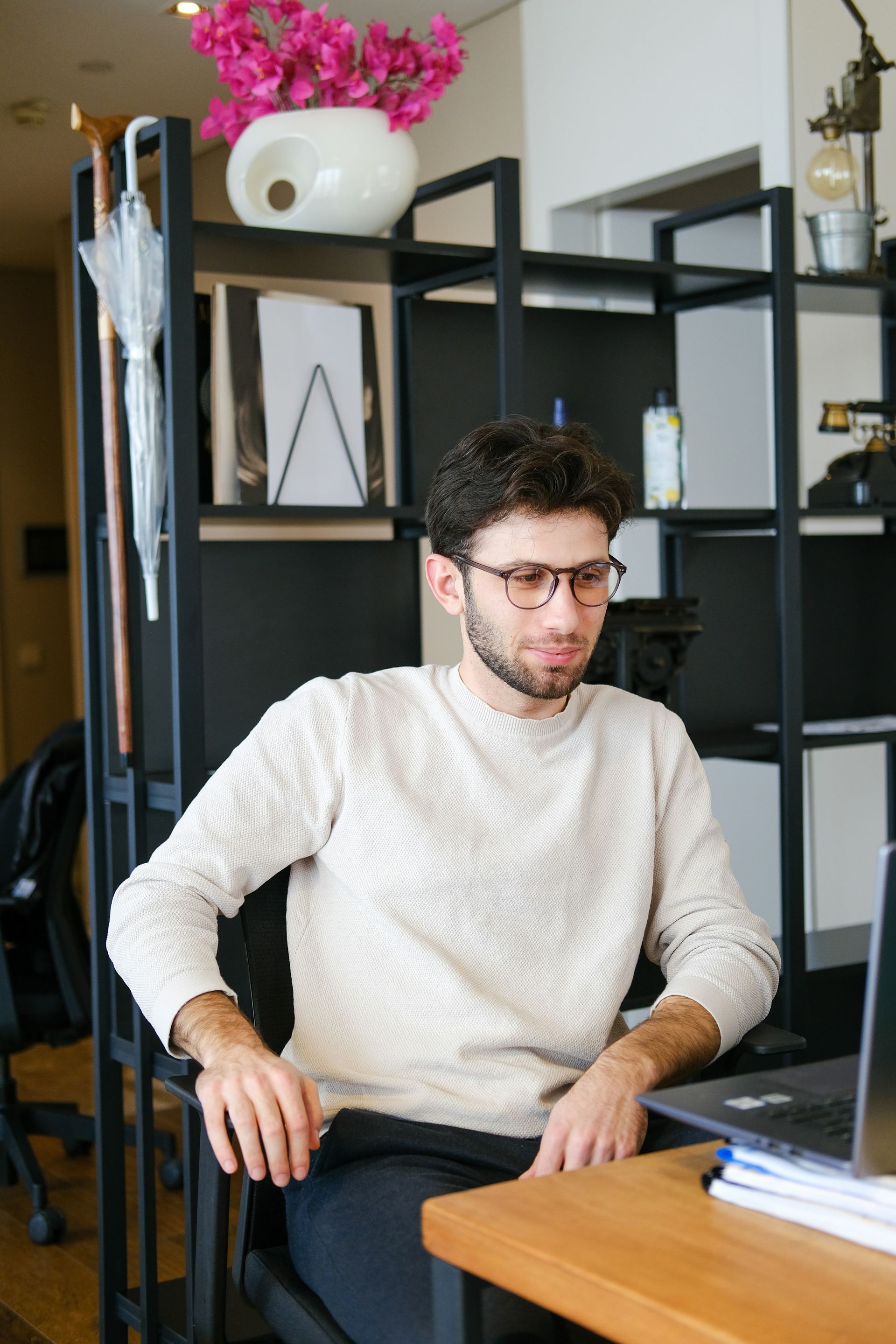A man wearing glasses is sitting at a desk with a laptop.