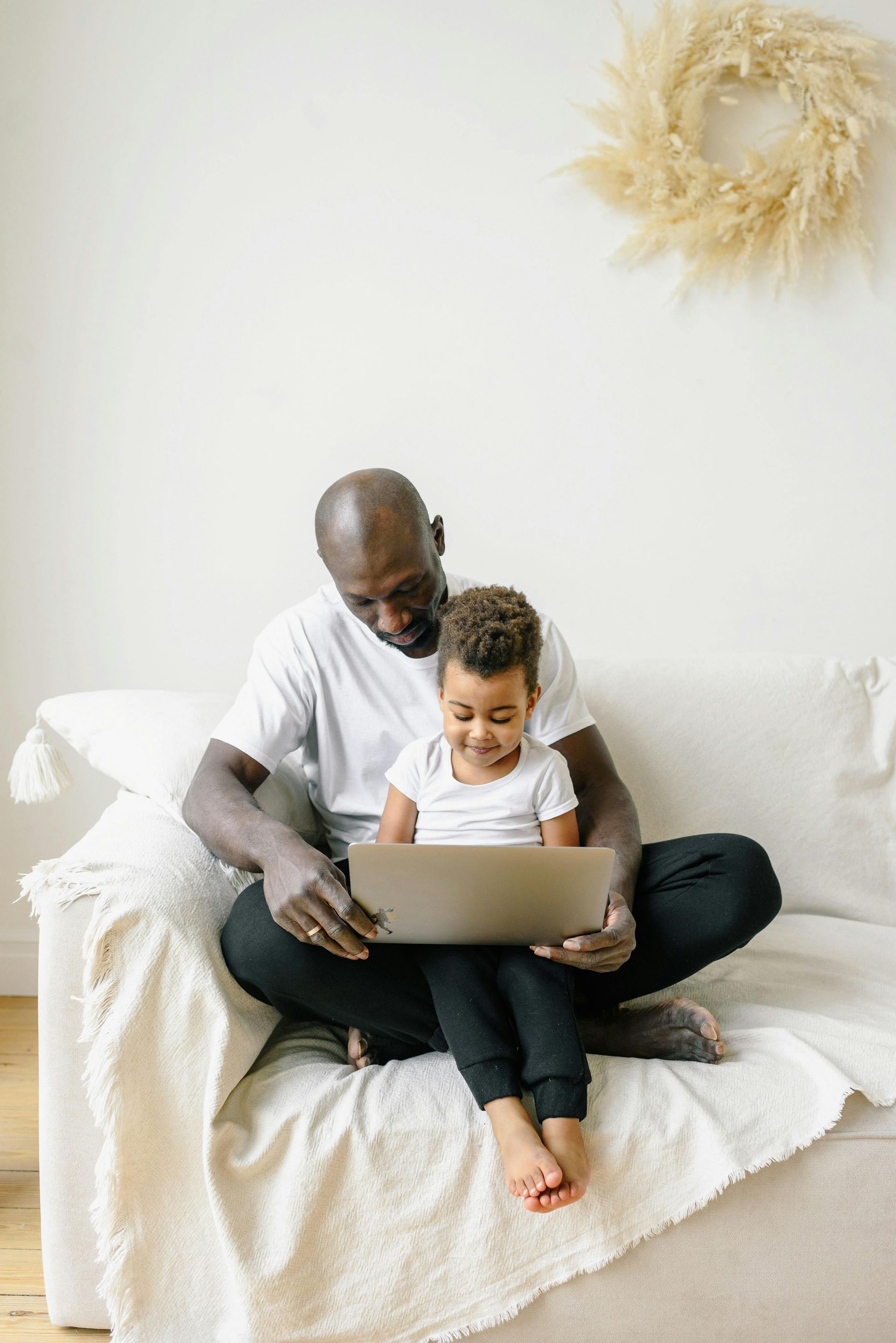 A man and a child are sitting on a couch looking at a laptop.