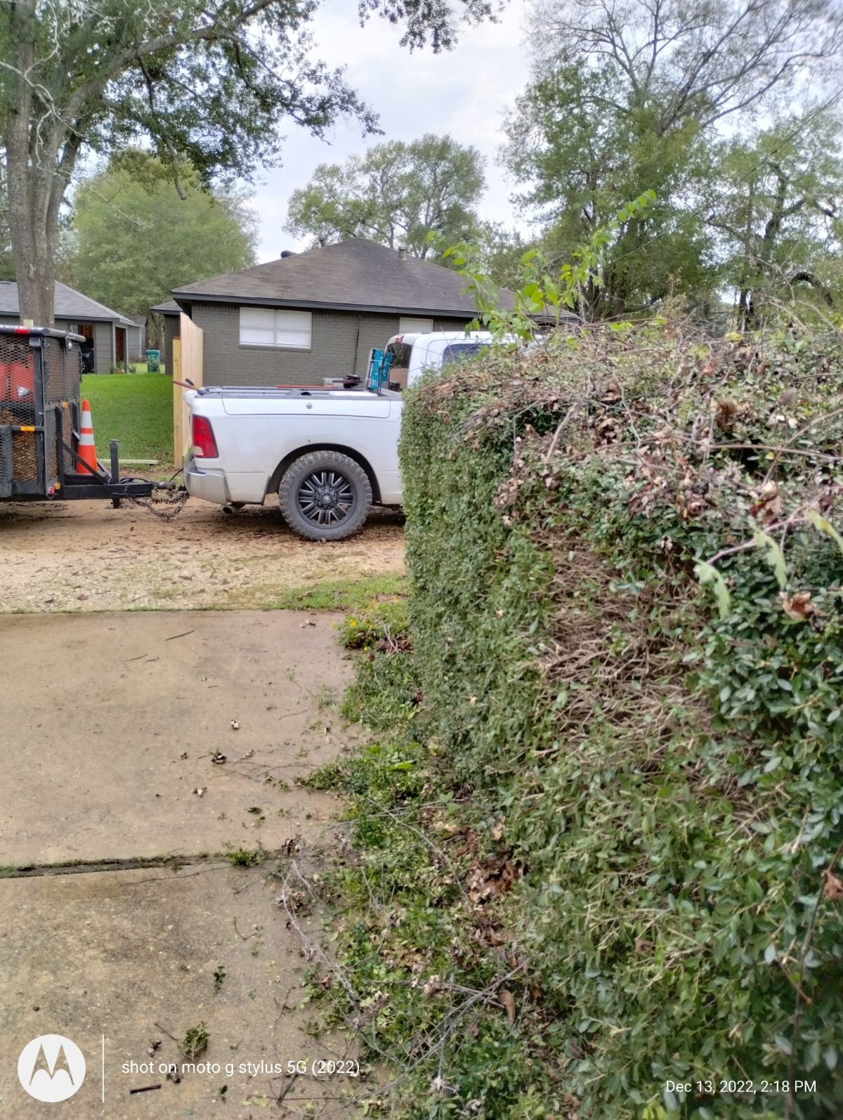 A white truck is parked next to a hedge in front of a house.