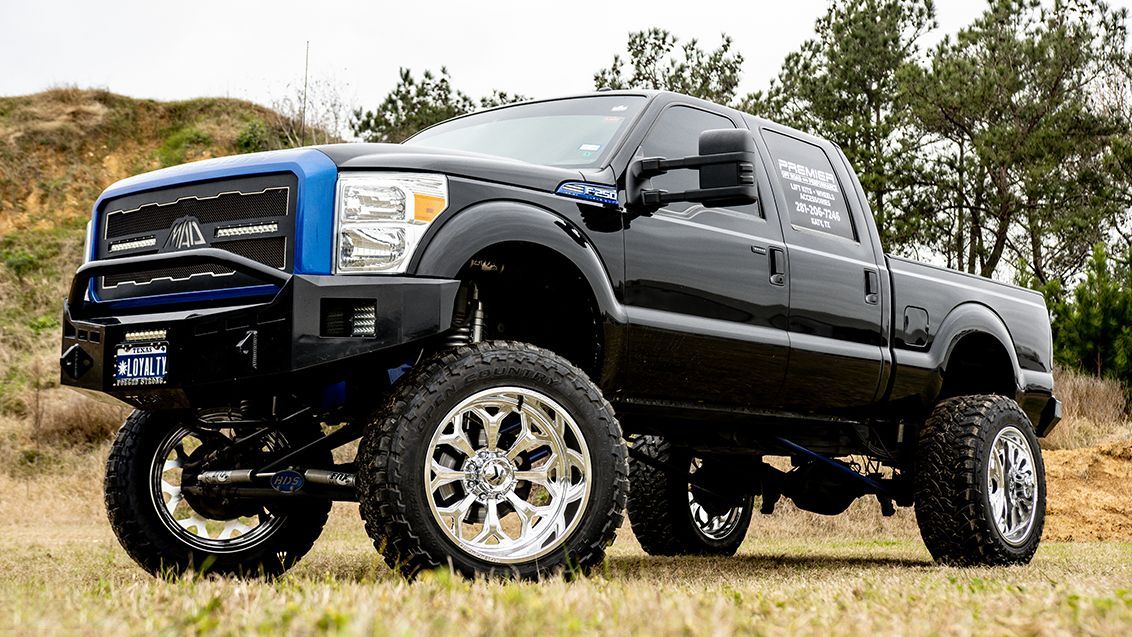 Lifted black pickup truck with chrome wheels parked on a grassy path near trees