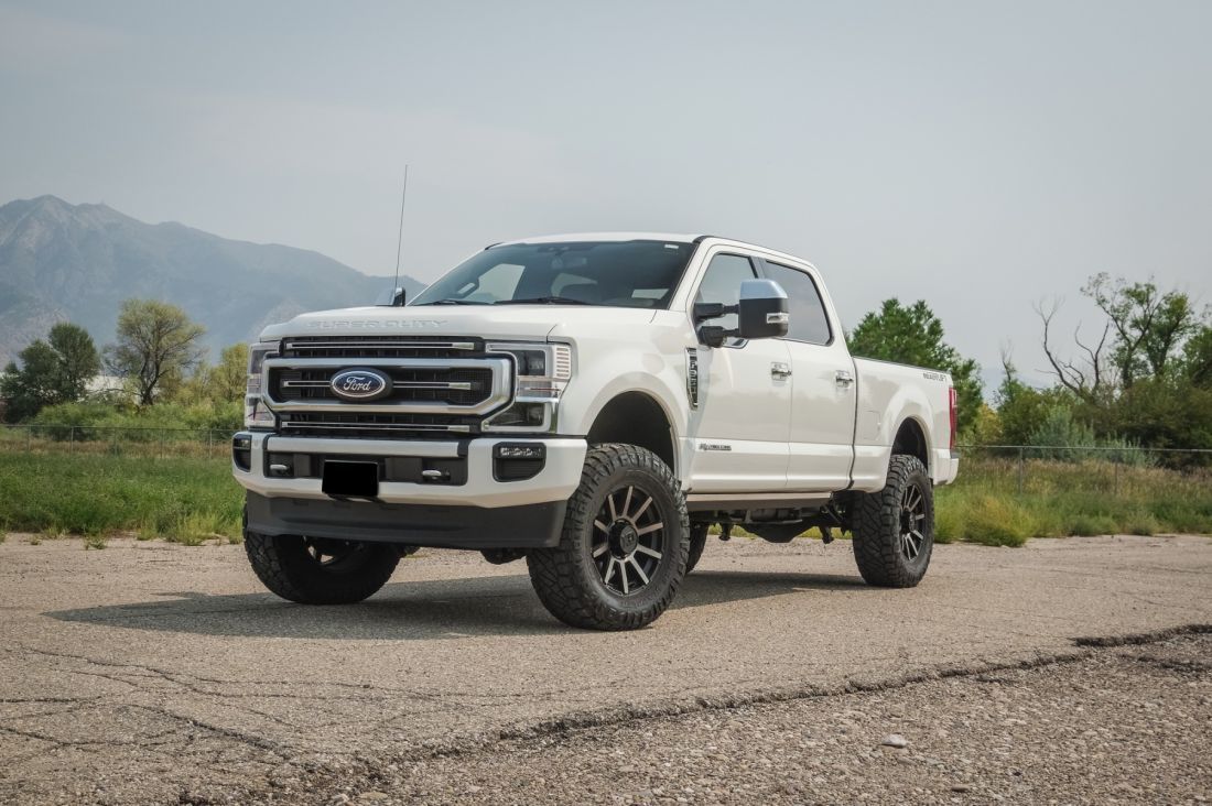 White Ford pickup truck parked on a gravel road with mountains in the background