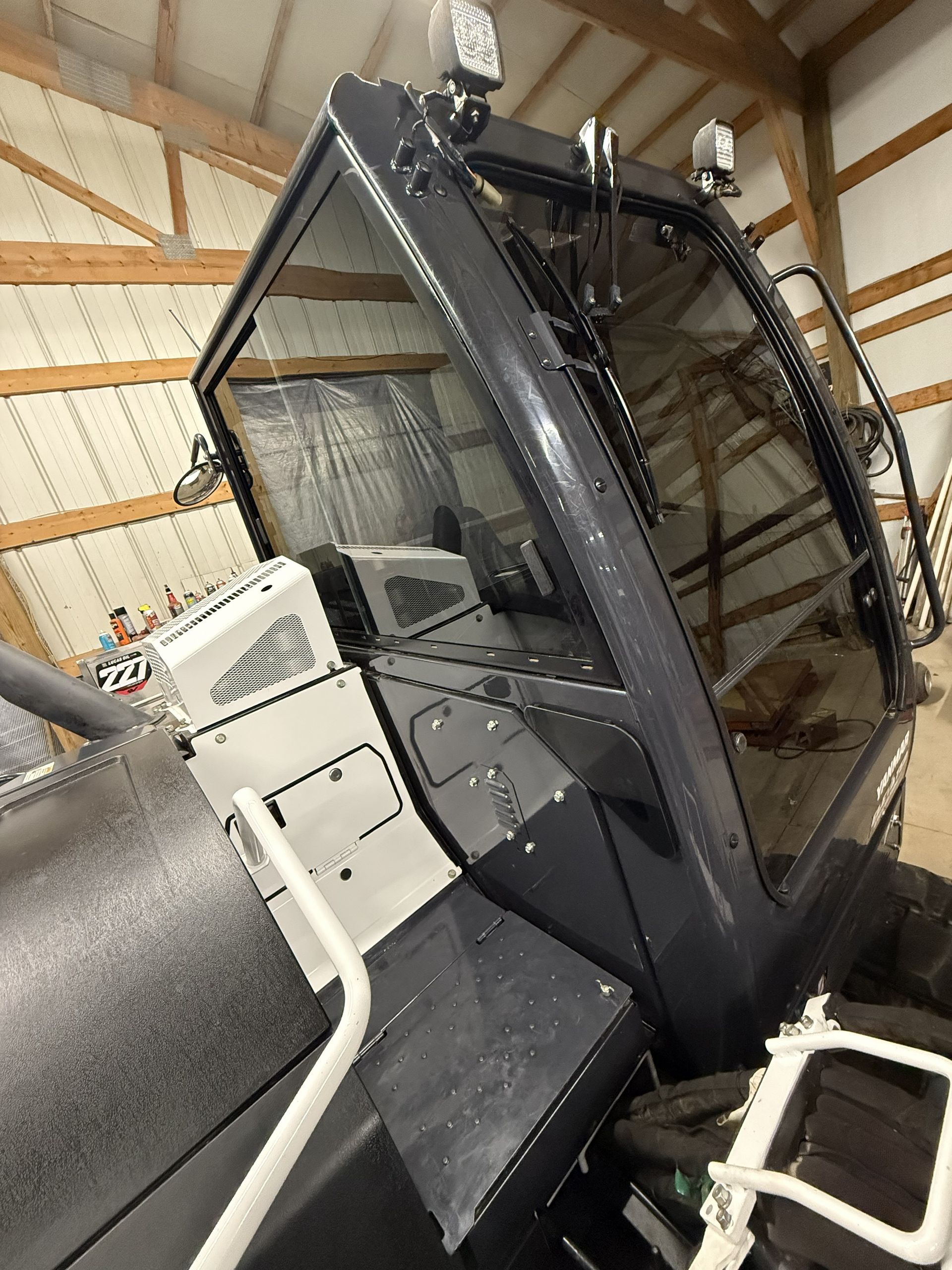 Large industrial machine with a dark glass enclosure in a workshop with exposed wooden beams.
