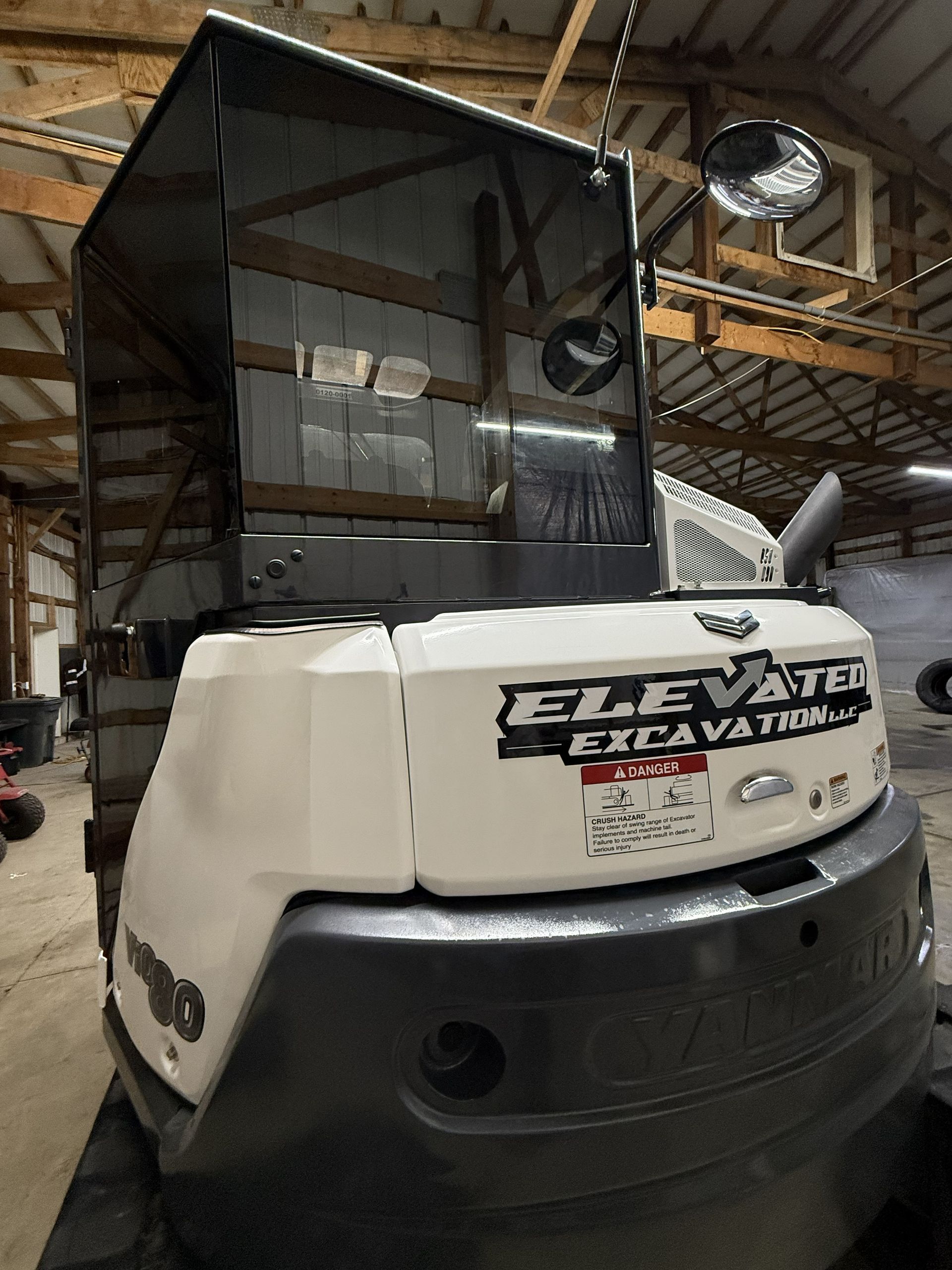 White-and-black Excavator machine inside a warehouse, with a raised cab and large front panel.