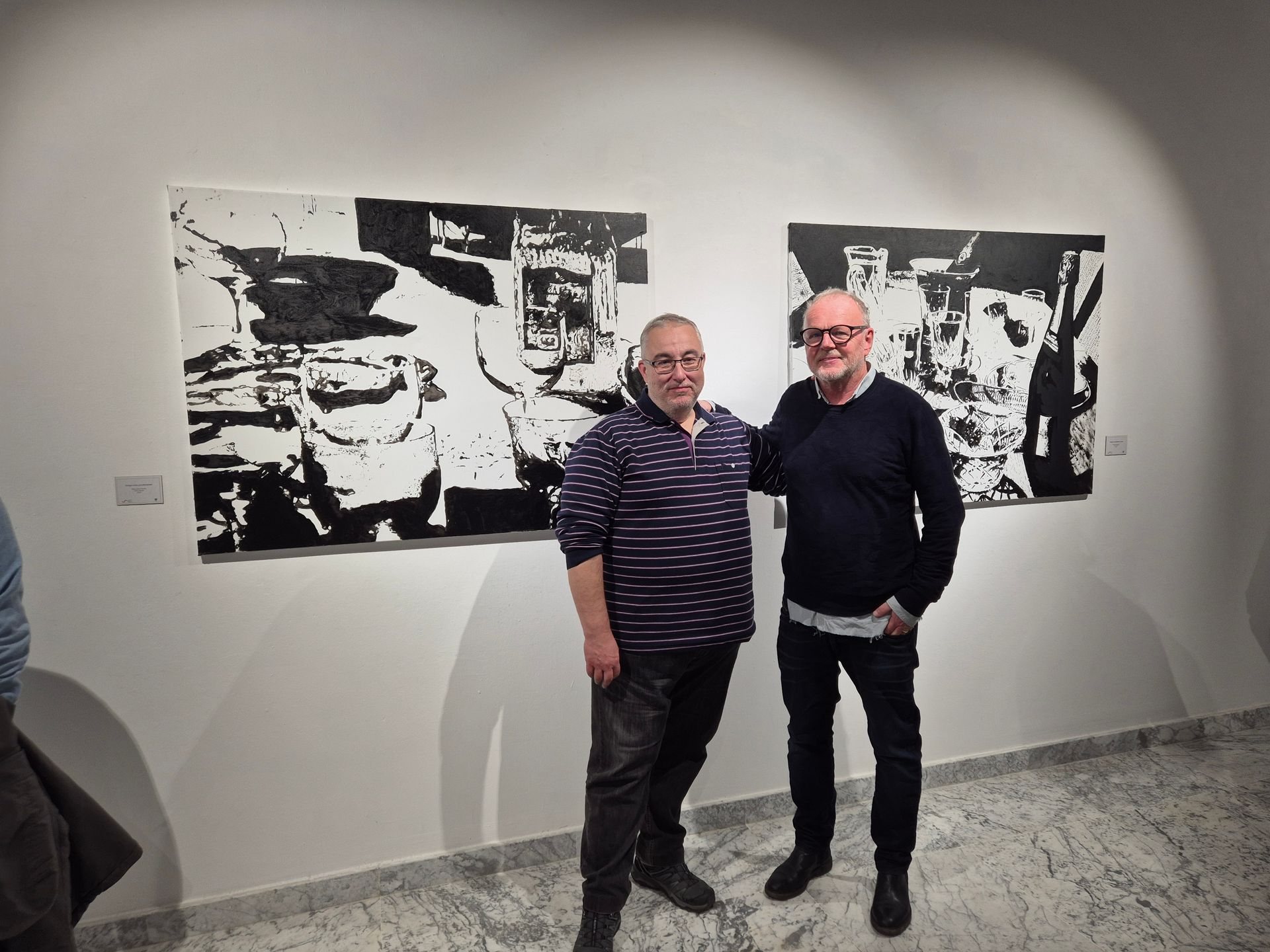 Dos hombres se encuentran cerca de dos pinturas abstractas en blanco y negro en una galería.
