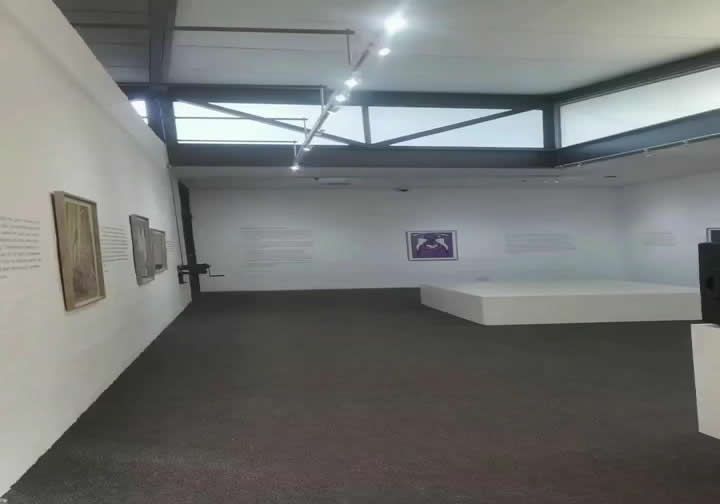 Una sala de exposiciones con  cuadros en las paredes.