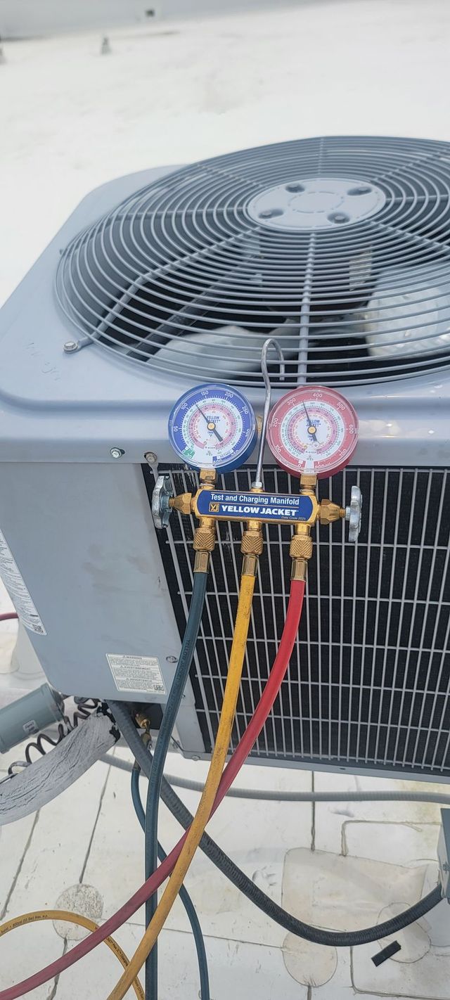 Technician using gauges to service an outdoor HVAC unit with a drill