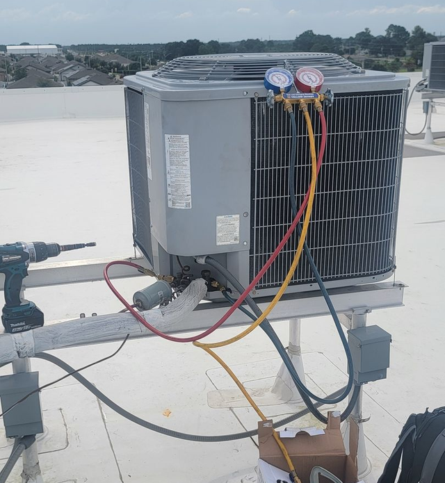 Two large outdoor HVAC condenser units with black grilles beside a building and greenery