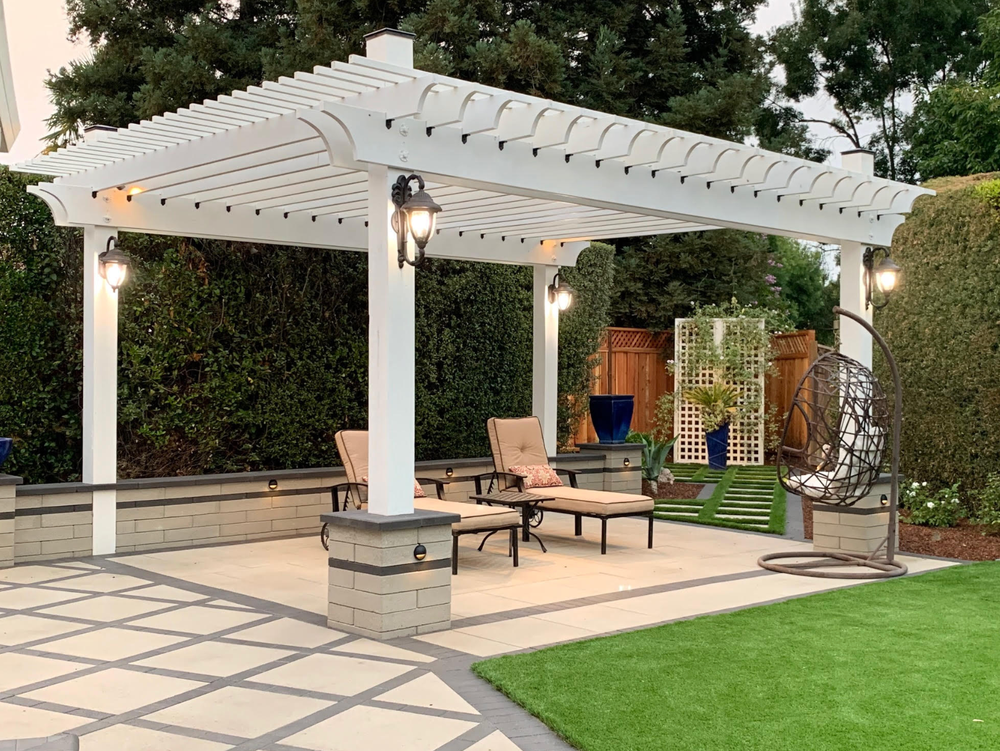 There is a pergola in the backyard with chairs underneath it.