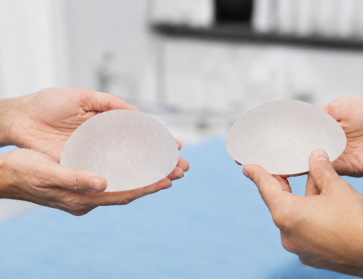 Mãos segurando implantes de silicone texturizados.