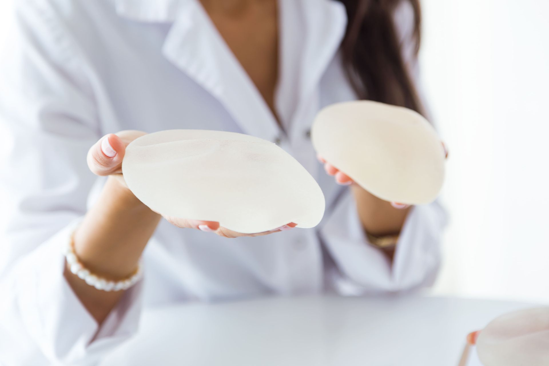 Médica de jaleco branco segurando duas próteses de silicone mamárias nas mãos, ilustração sobre implantes de silicone