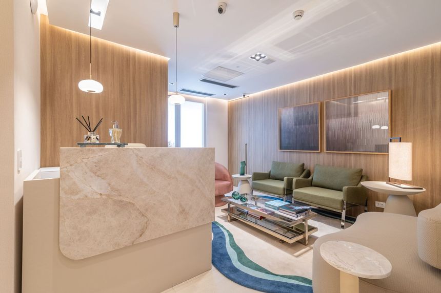 Lobby de hotel moderno em tons de bege com balcão de recepção em mármore, sofás verdes e iluminação suave com pendentes.