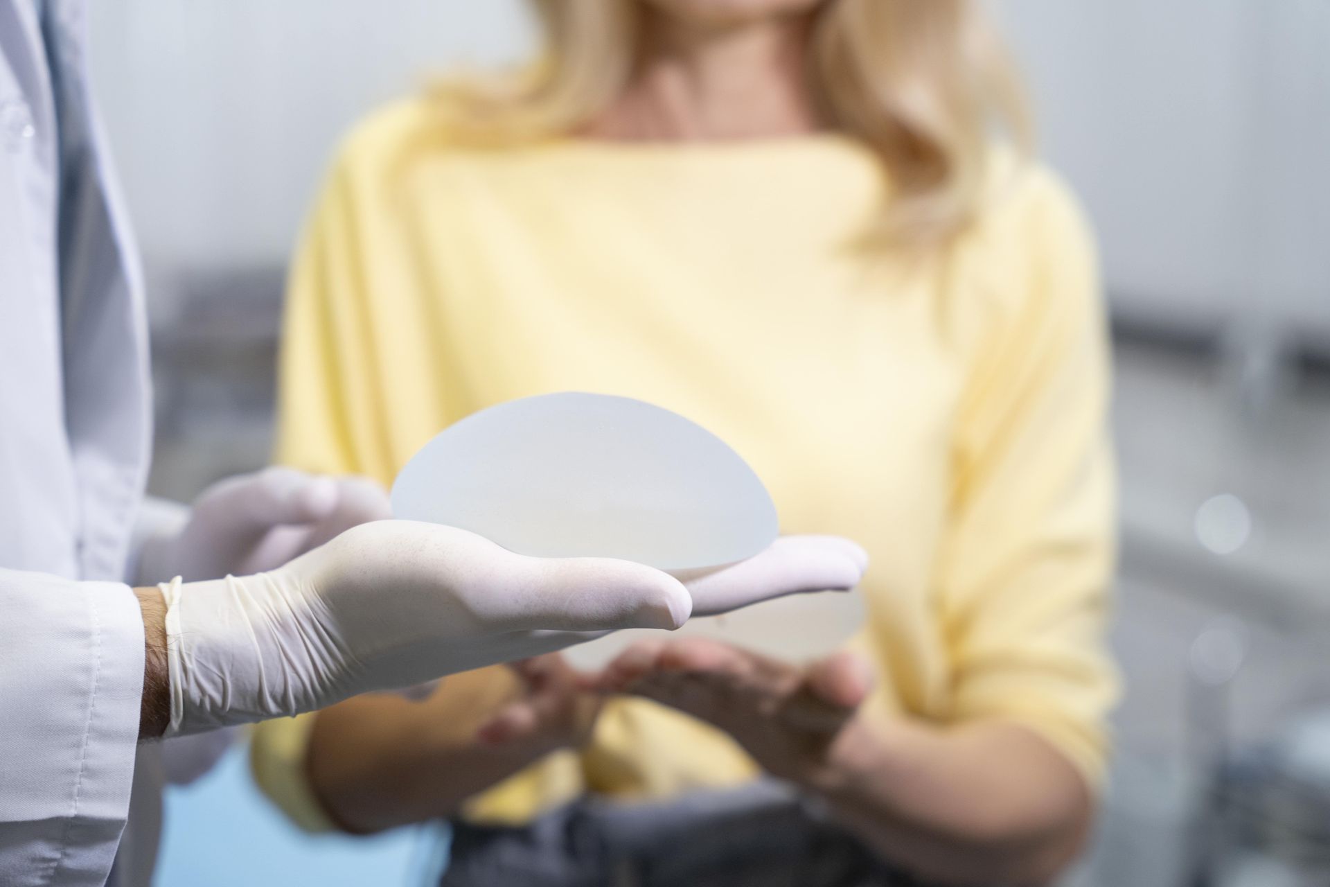Cirurgiã plástica segurando prótese de silicone mamária diante de paciente durante consulta