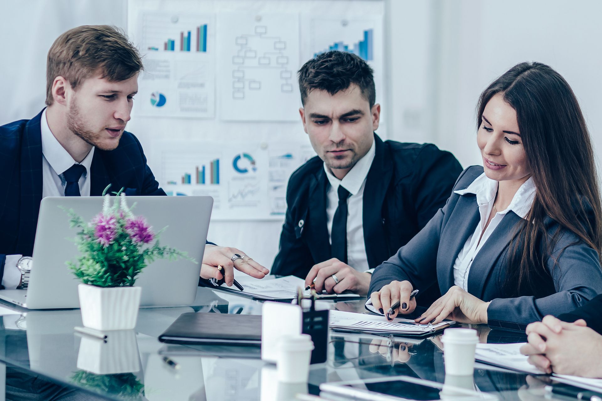 a group of business people are sitting around a table looking at a laptop .