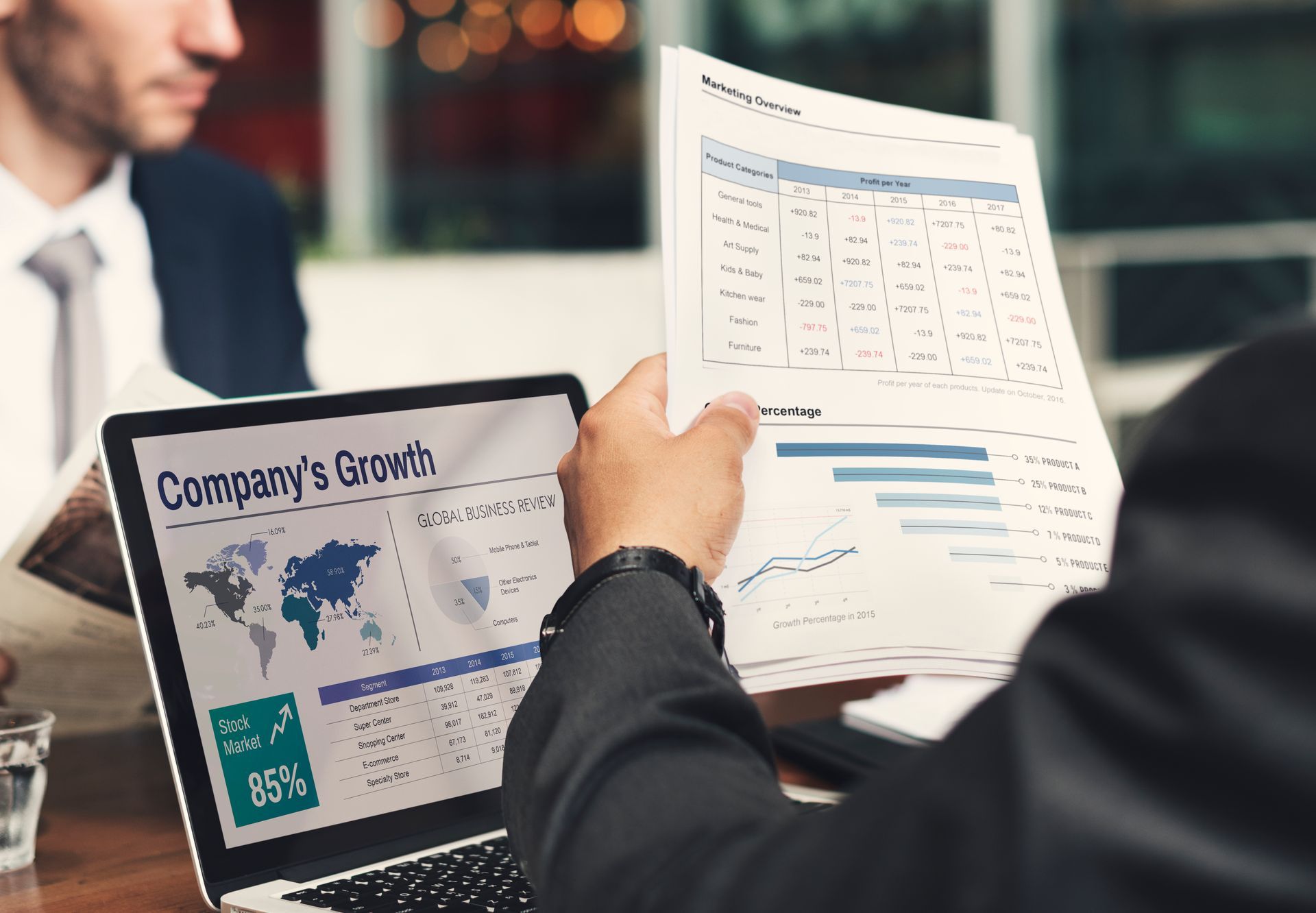 Businesspeople reviewing charts and graphs displayed on a laptop and paper documents in an office.