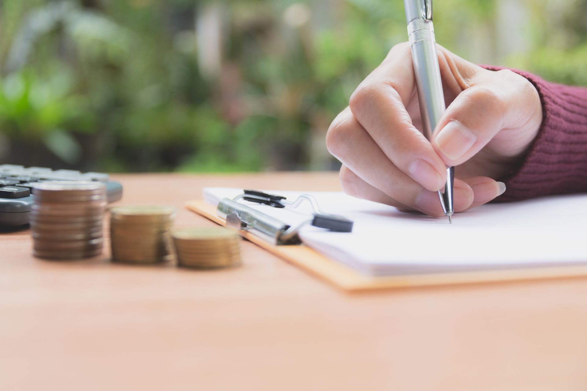 Person writing on notepad with coins and calculator in the background.