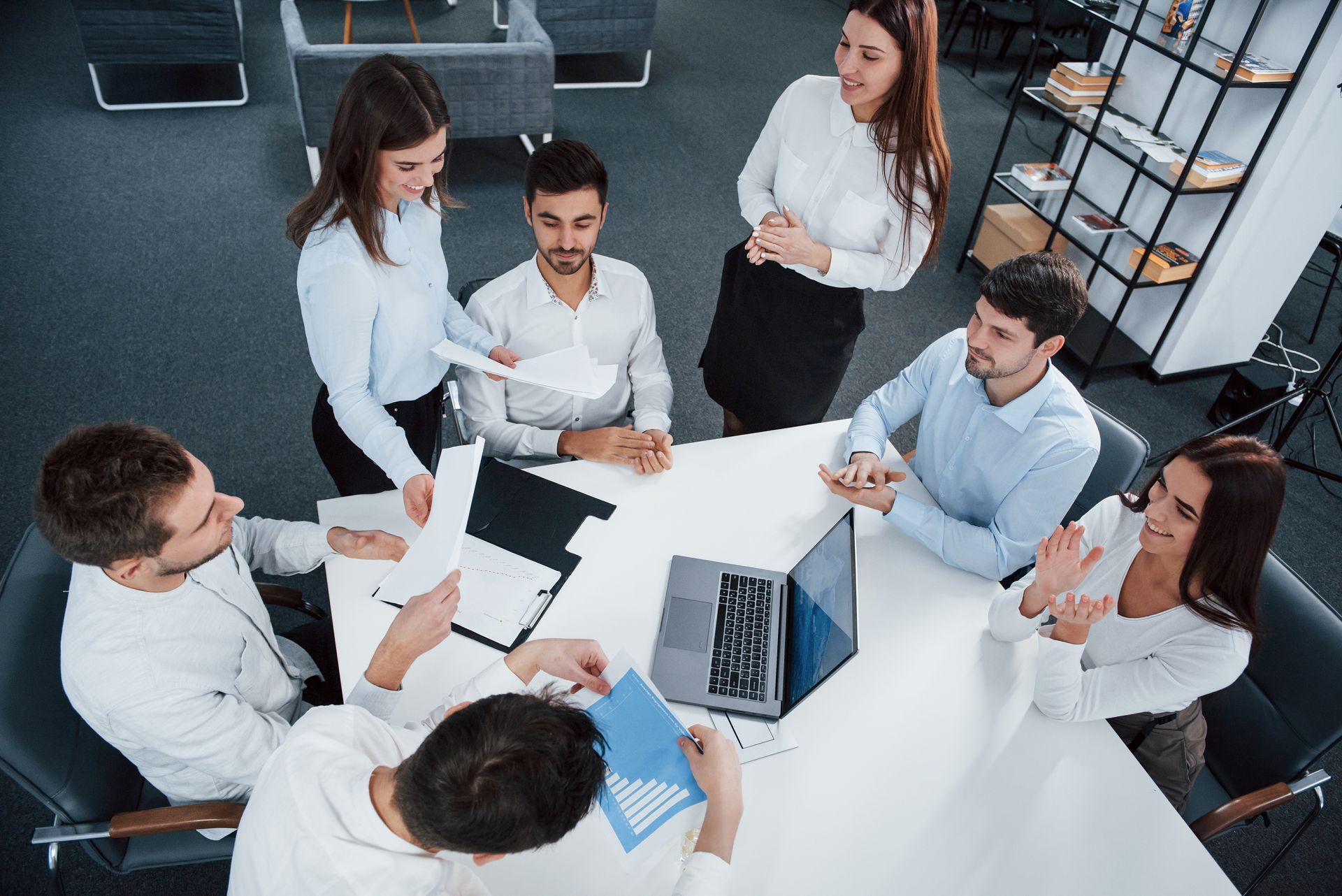 a group of people are sitting around a table with a laptop .