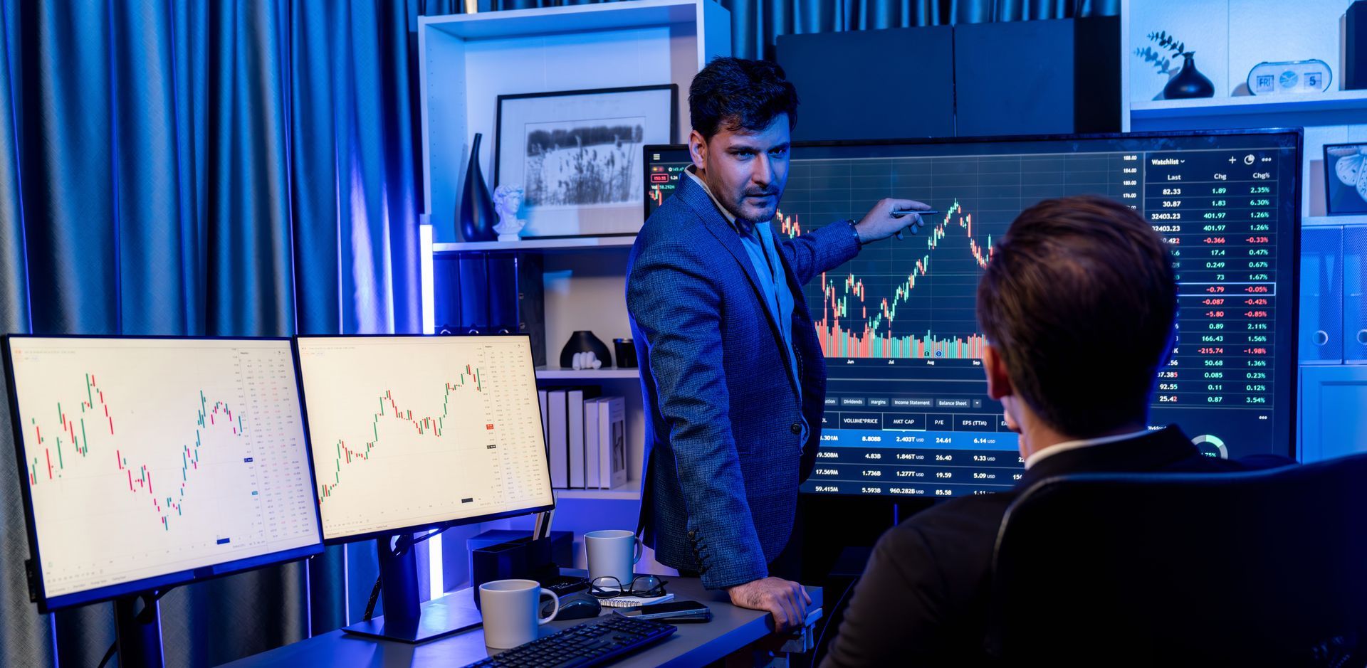 A man is standing next to a man sitting in front of a computer screen.
