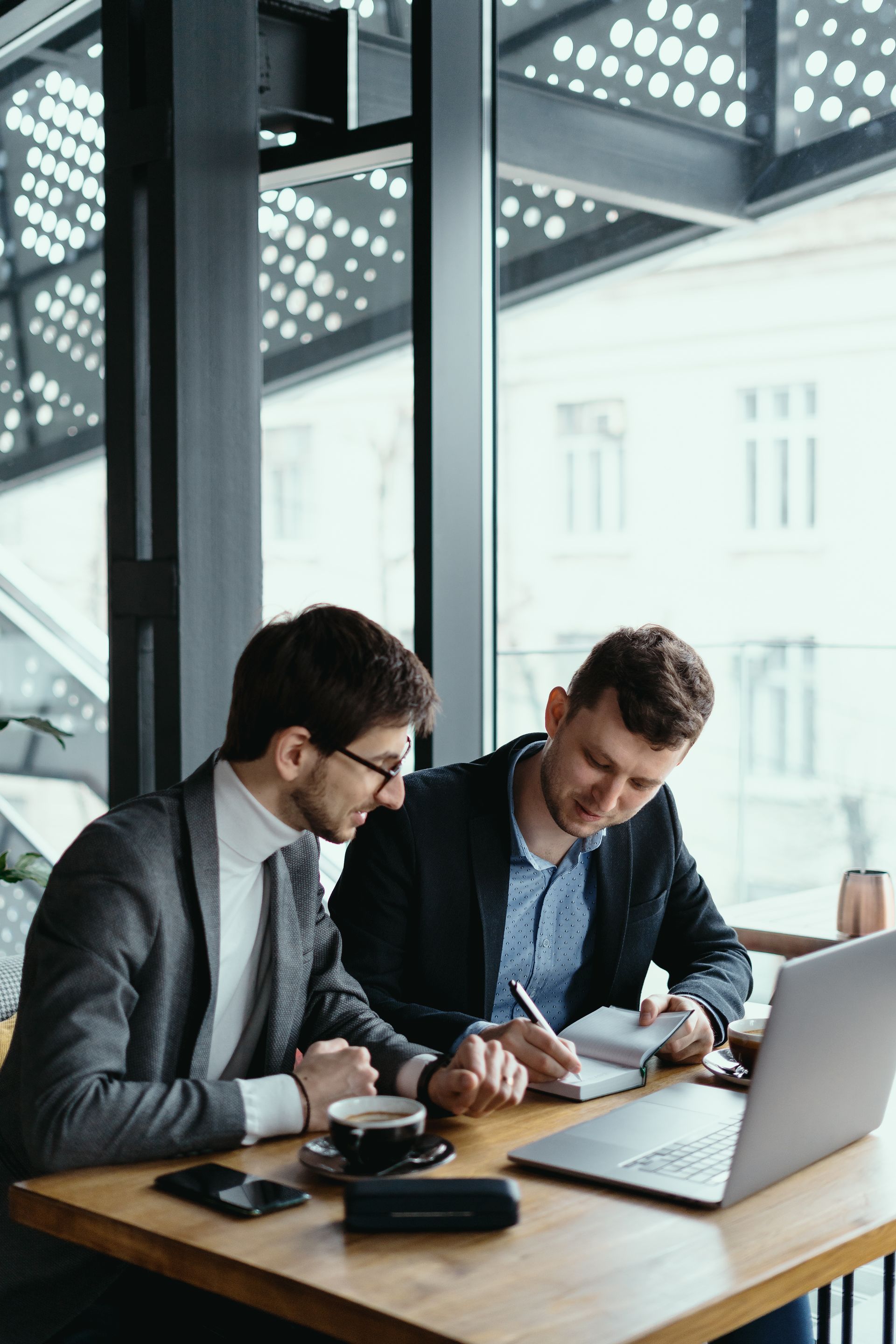 two men are sitting at a table with a laptop and a cup of coffee .
