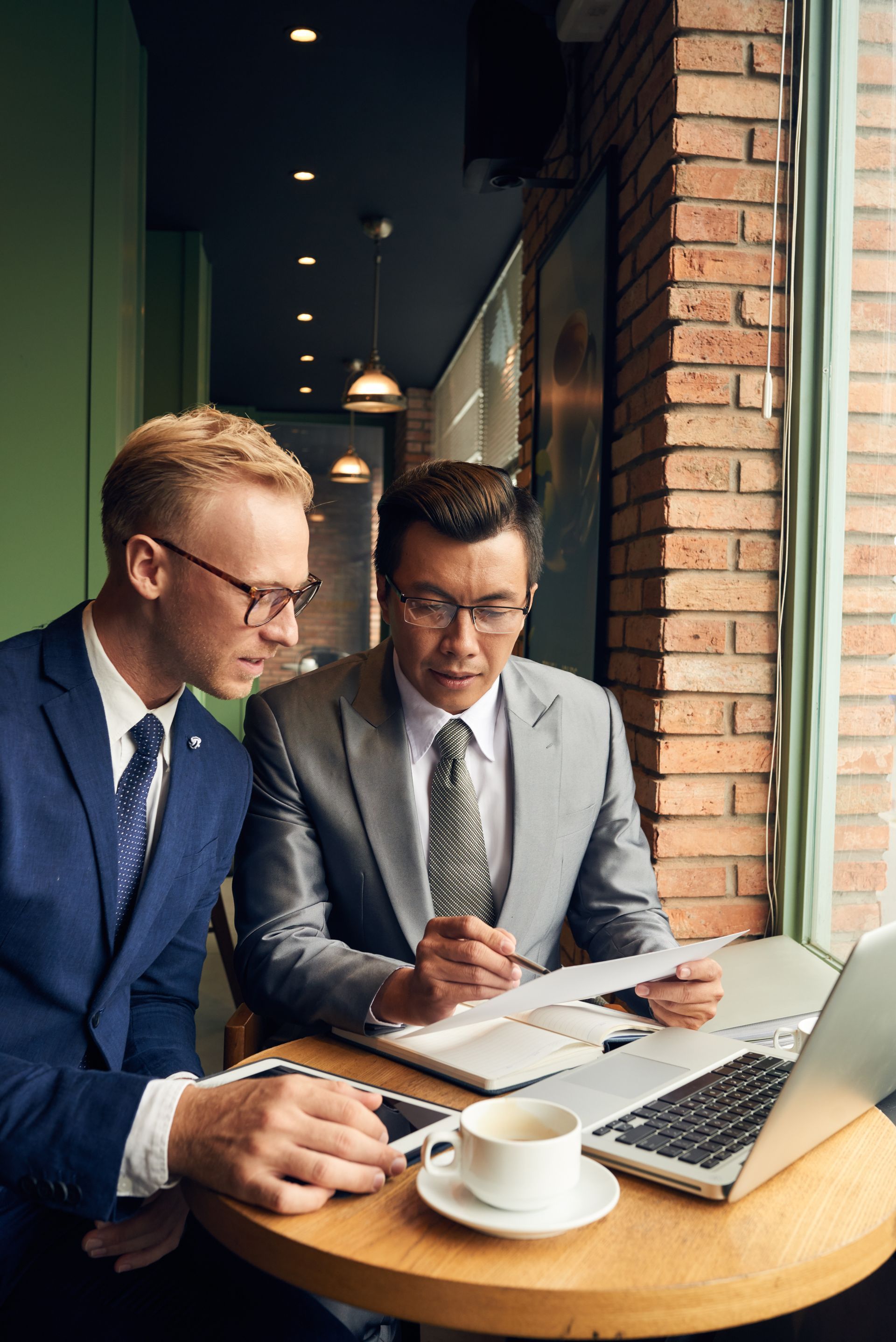 two men are sitting at a table looking at a laptop .