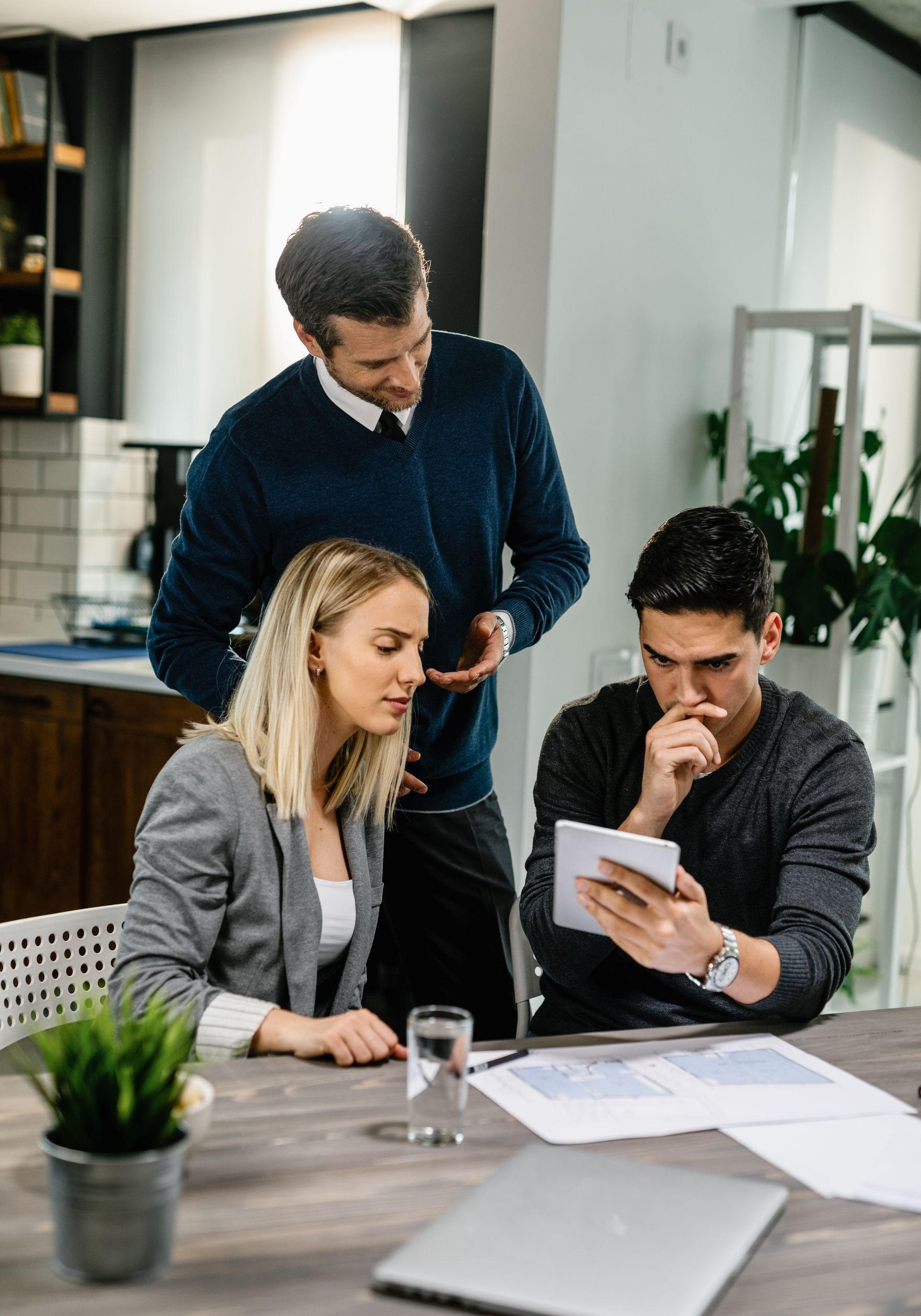 a group of people are sitting at a table looking at a tablet .
