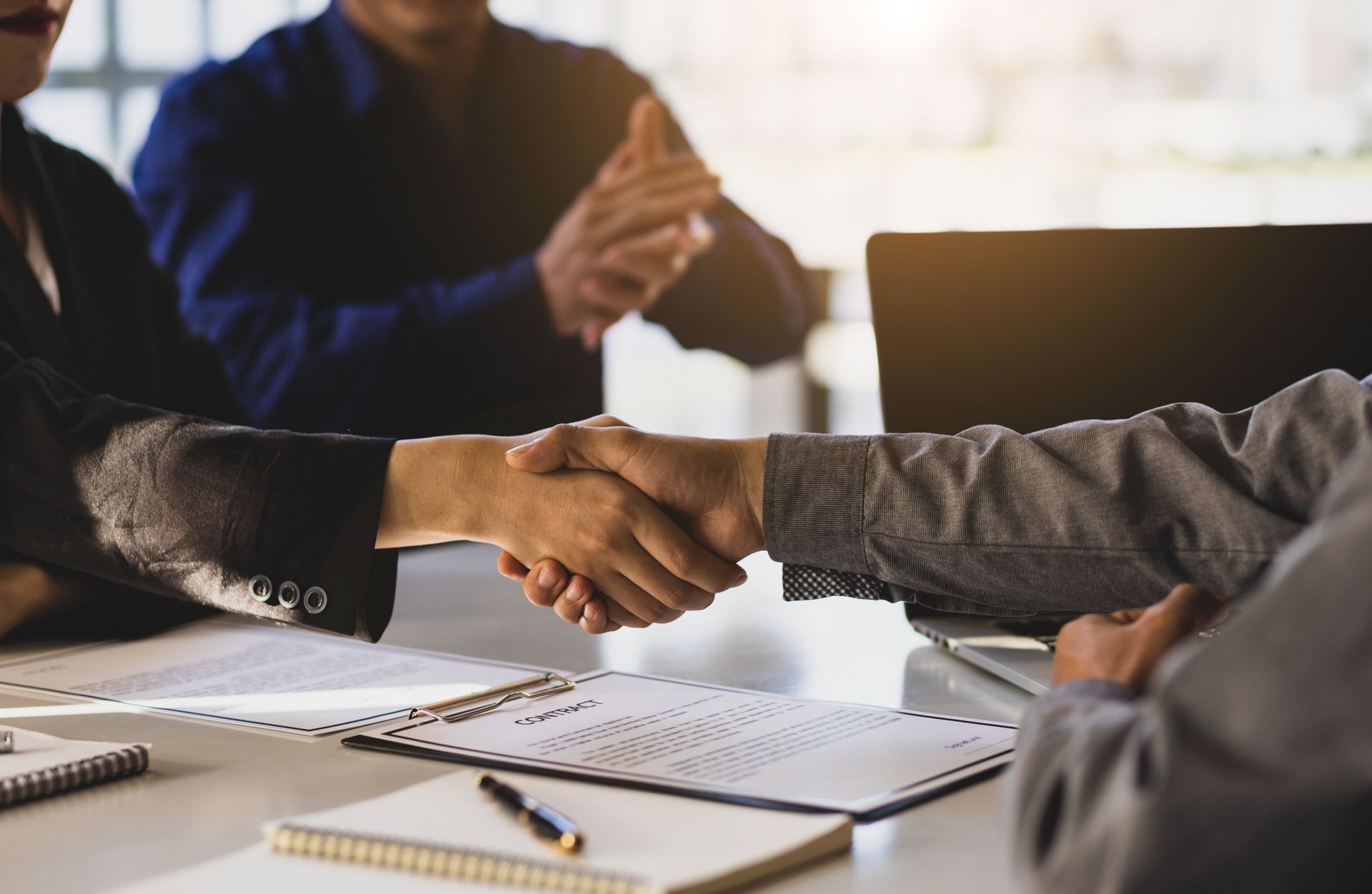 Businesspeople shaking hands across a desk with papers and notebooks in a meeting room