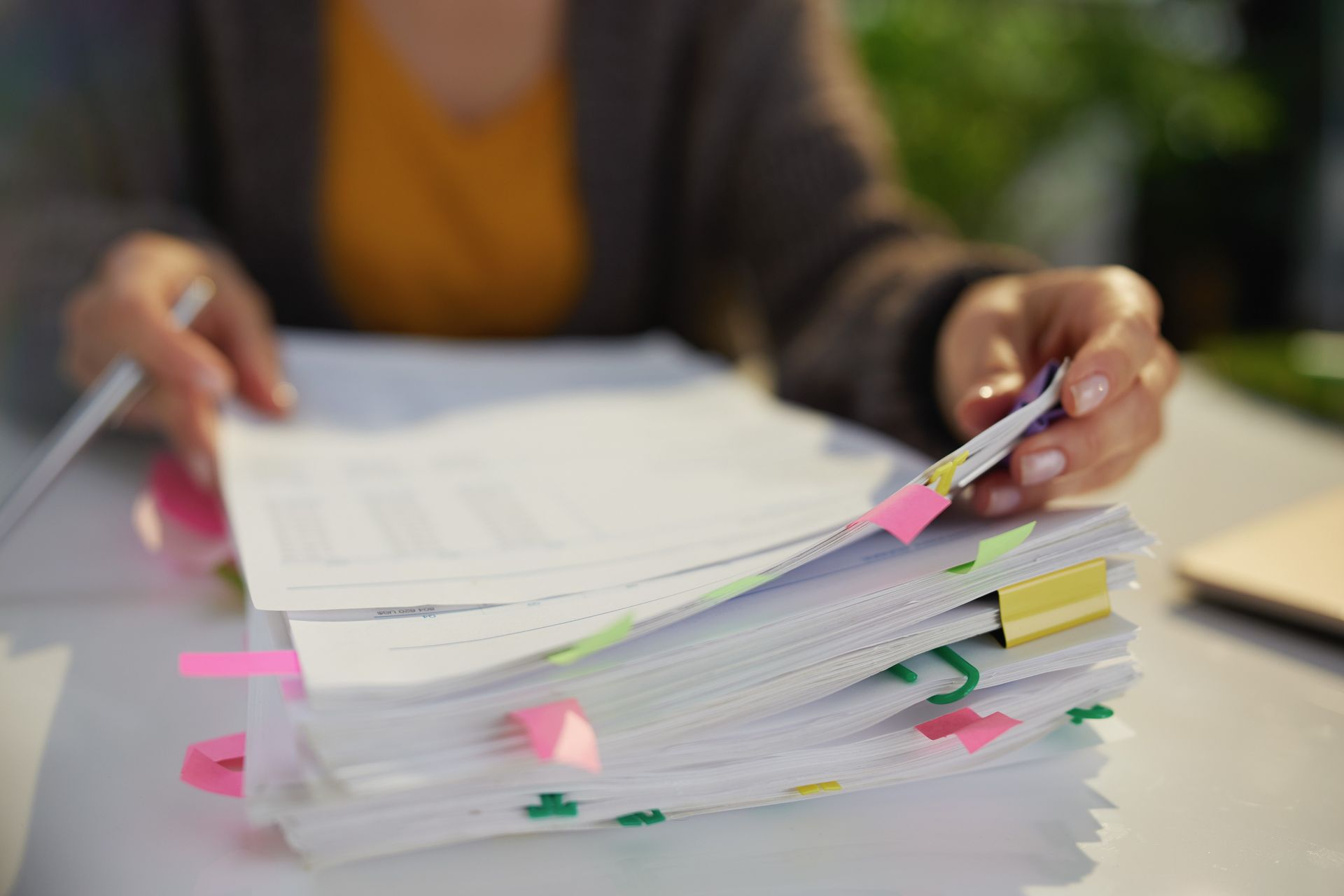 Hands sorting a stack of papers with colorful sticky tabs on a desk