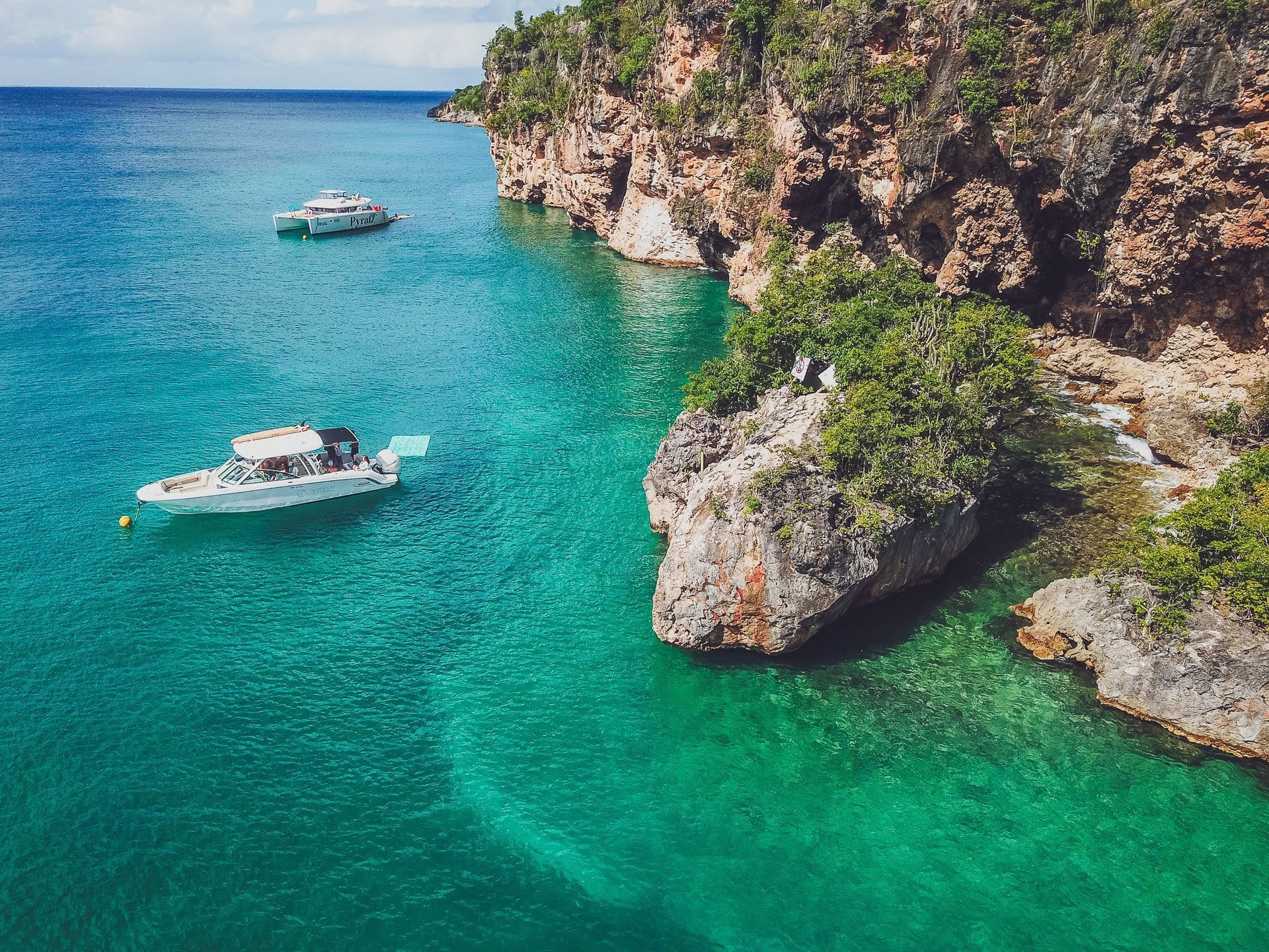 A boat is floating on top of a body of water next to a cliff.
