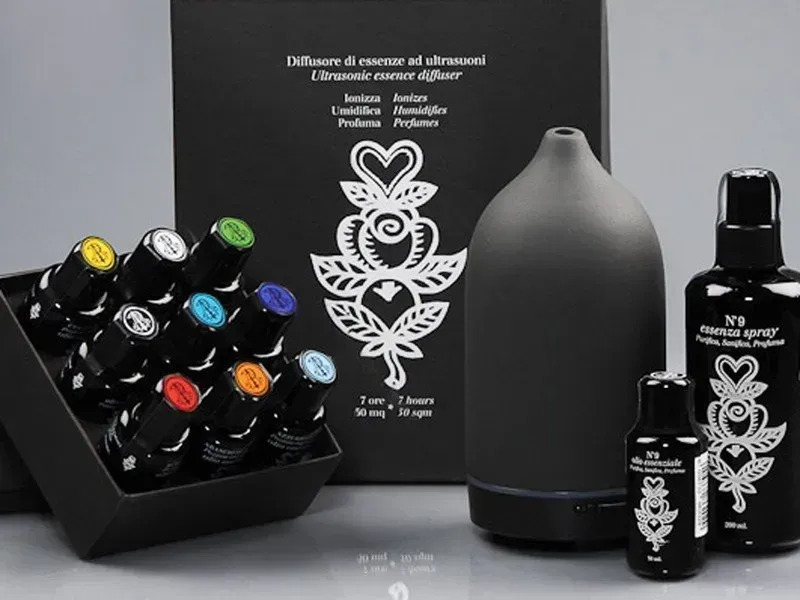 Flaconi e tubetti neri per prodotti per la cura della pelle con etichette floreali in mostra accanto a un diffusore grigio.