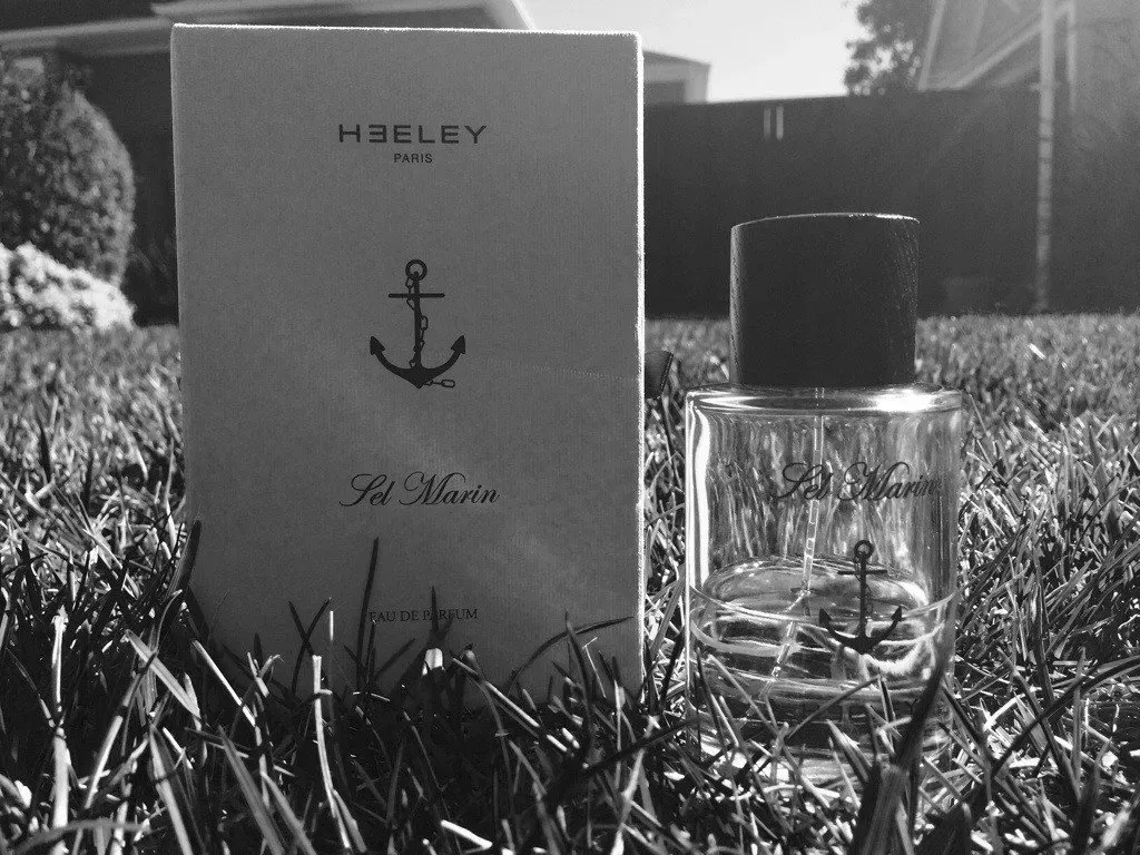 Flacone e scatola di profumo monocromatici in un prato all'aperto con una recinzione sullo sfondo.