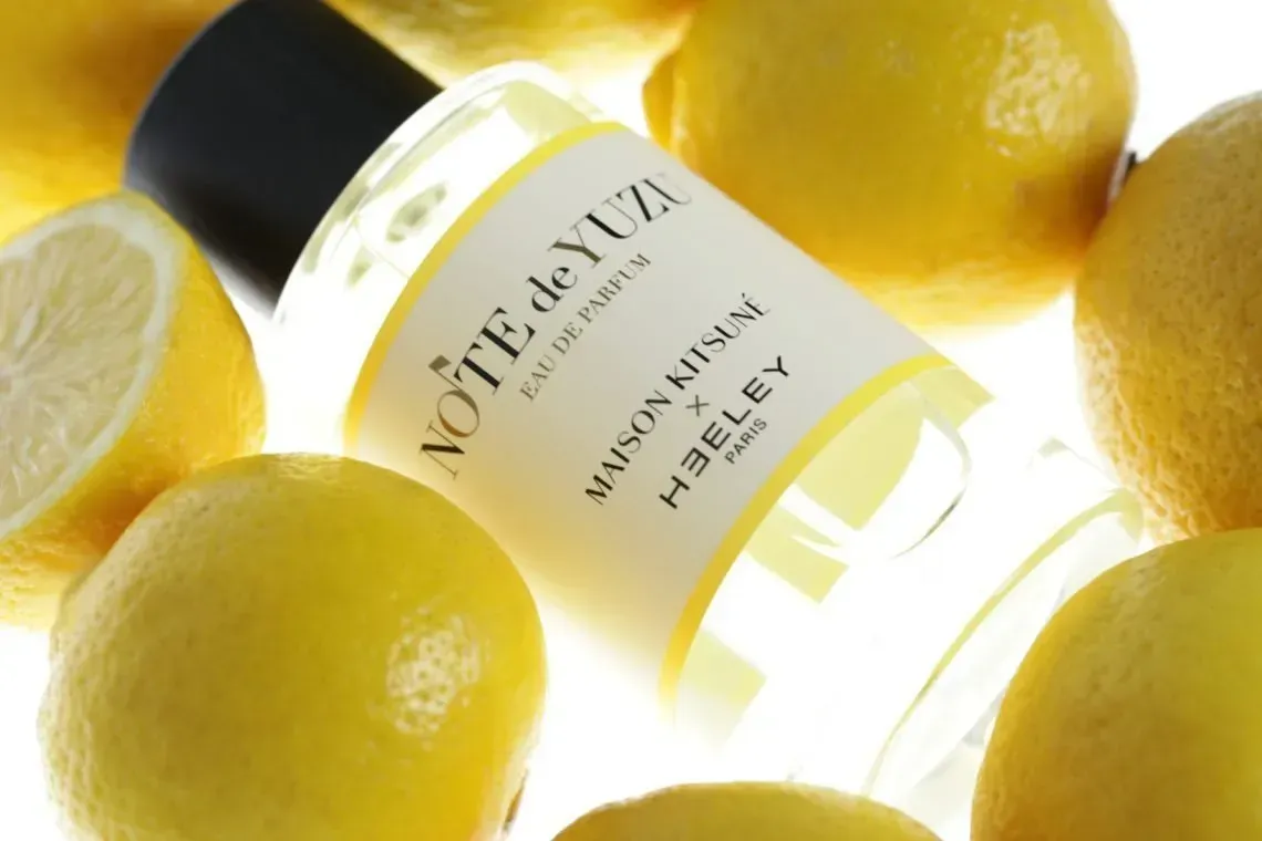 Limoni gialli intorno a una bottiglia di profumo bianca inclinata con l'etichetta 