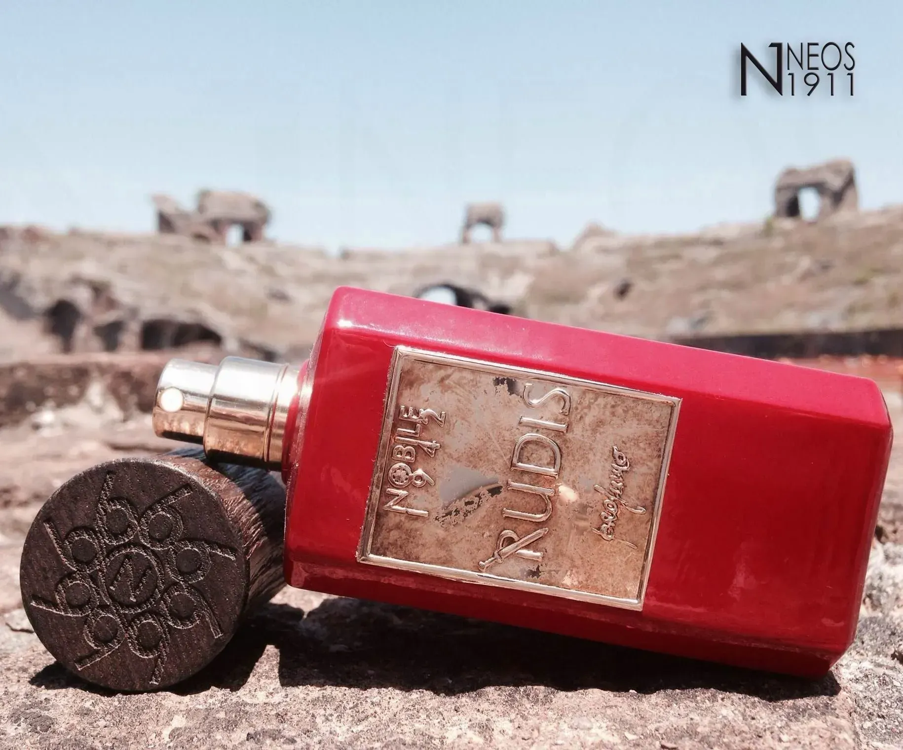 Una boccetta di profumo rossa giace su un terreno roccioso in un ambiente simile a un deserto.