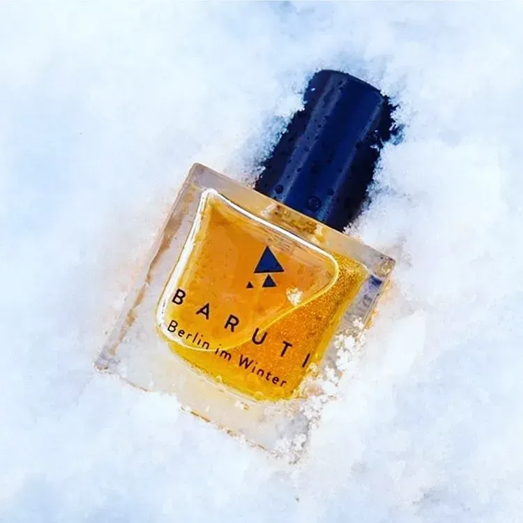 Flacone di profumo BARUTI color ambra con tappo blu scuro, spolverato di neve su sfondo bianco.