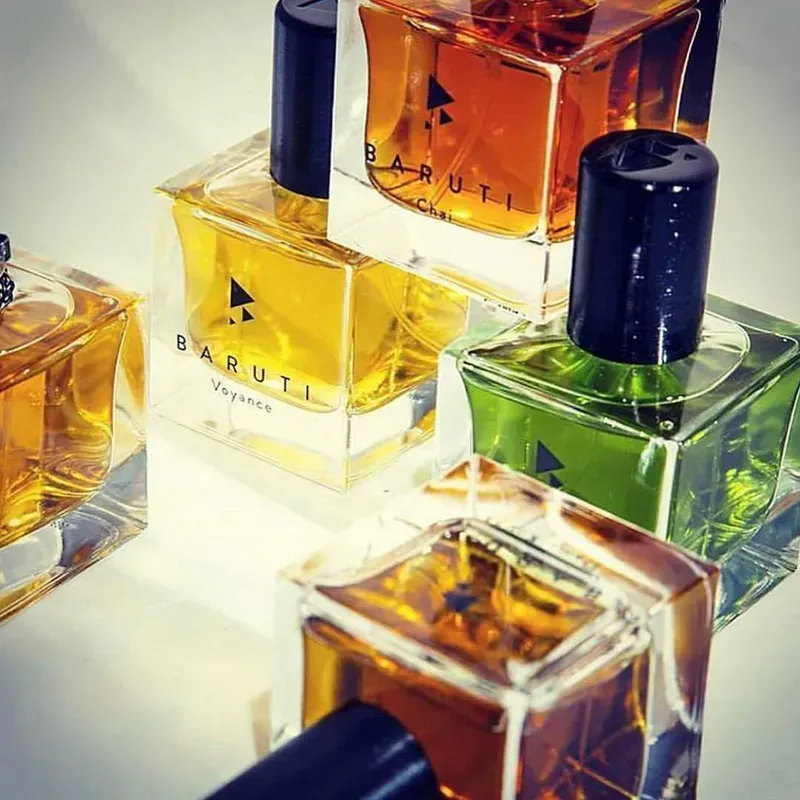 Assortimento di flaconi di profumo colorati con tappi scuri, disposti su una superficie riflettente luminosa.