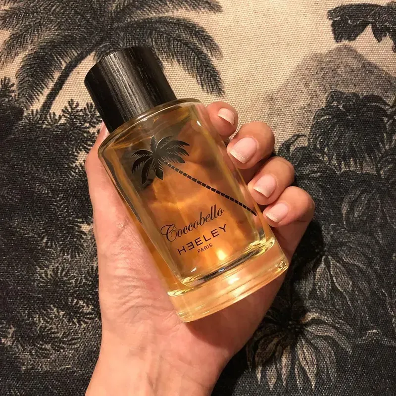 Mano che regge una bottiglia di Hennessy all'ananas sullo sfondo di una composizione di foglie tropicali.