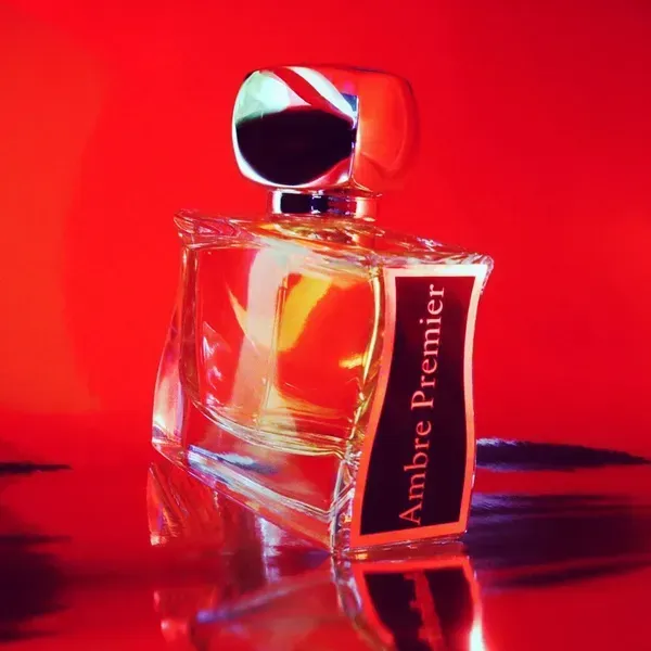 Flacone di profumo Premier color ambra su sfondo rosso acceso, con tappo a specchio e riflesso