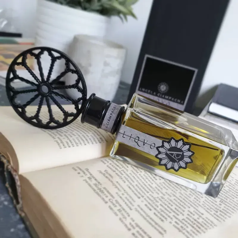 Flacone di profumo decorativo su un libro aperto accanto a una candela e una scatola nera.
