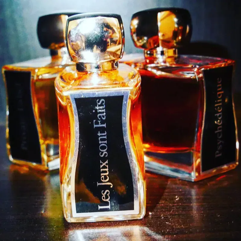 Tre flaconi di profumo color ambra su una superficie scura, con la scritta 