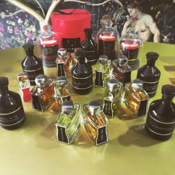Diverse bottiglie di vetro contenenti profumi o estratti liquidi, disposte su un tavolo con uno sfondo floreale.