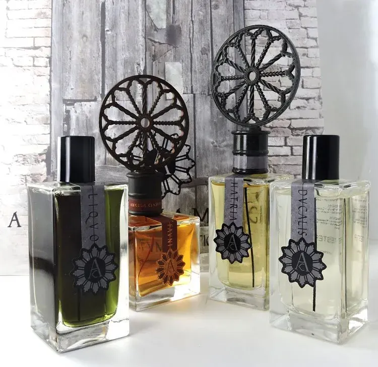 Quattro flaconi di profumo decorativi con tappi floreali neri, disposti su una superficie bianca contro