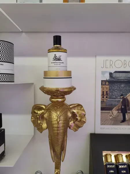 Espositore dorato a forma di elefante con una boccetta di profumo su uno scaffale, accanto a scatole di prodotti impilate.