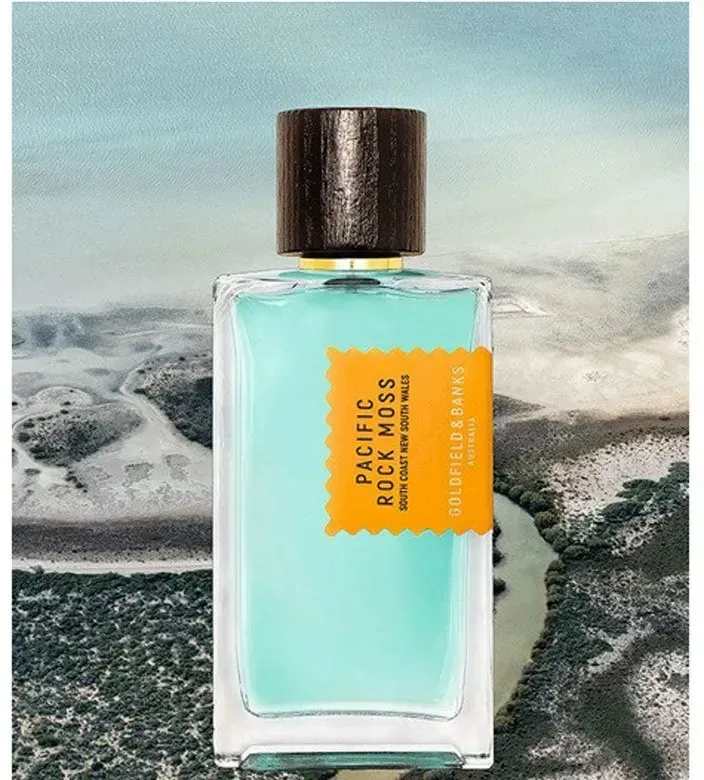 Flacone di profumo turchese con tappo scuro ed etichetta arancione su uno sfondo di mare nuvoloso.