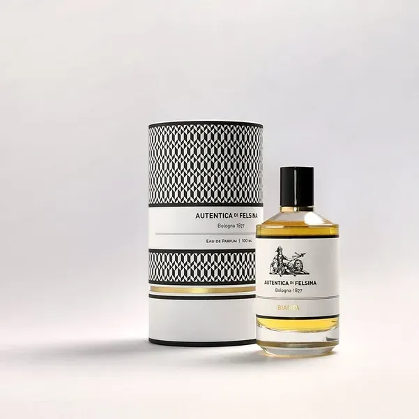 Flacone di profumo e scatola cilindrica abbinata con decorazioni a motivi neri e dorati su sfondo bianco.
