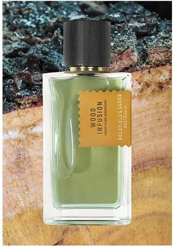 Flacone di profumo verde con tappo nero ed etichetta arancione su sfondo effetto pietra.