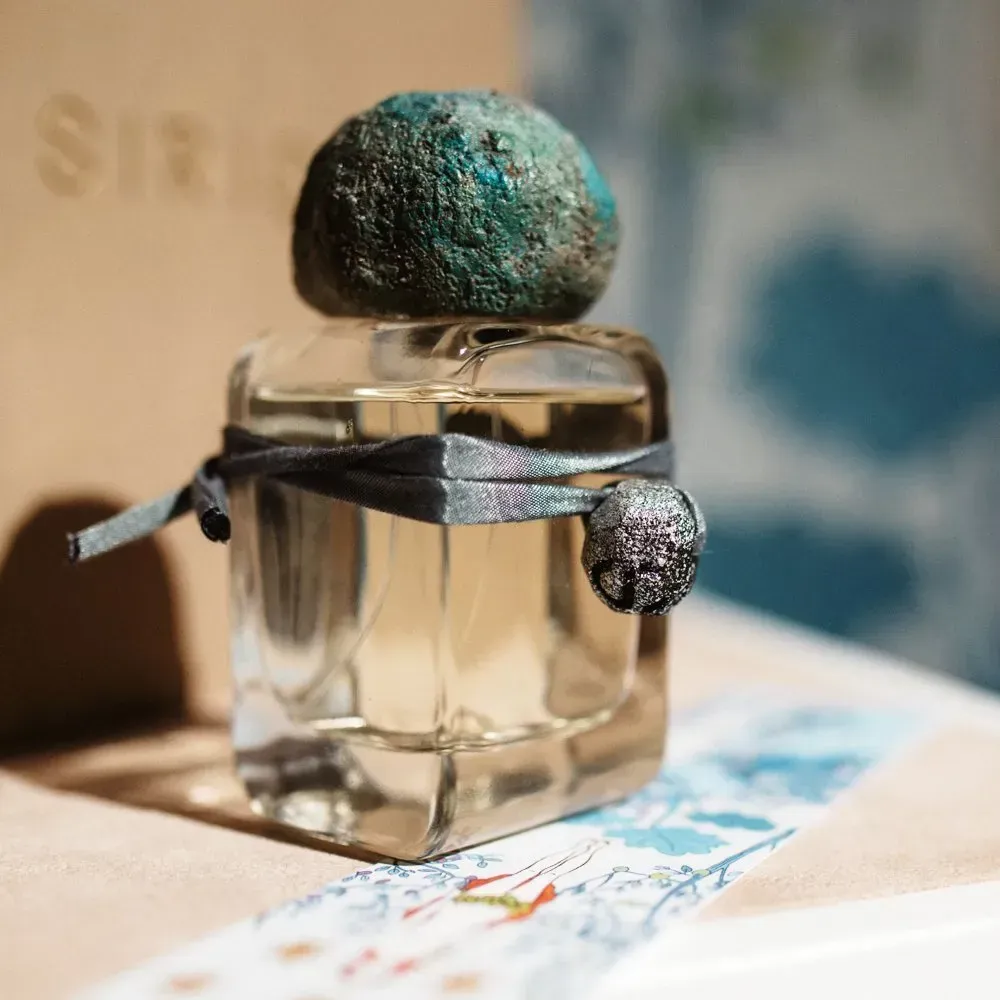 Flacone di profumo trasparente con tappo scuro dalla texture particolare e nastro