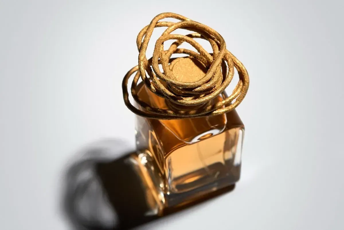 Oggetto dorato a forma di anello su una piccola bottiglia di profumo in vetro ambrato con un'ombra delicata