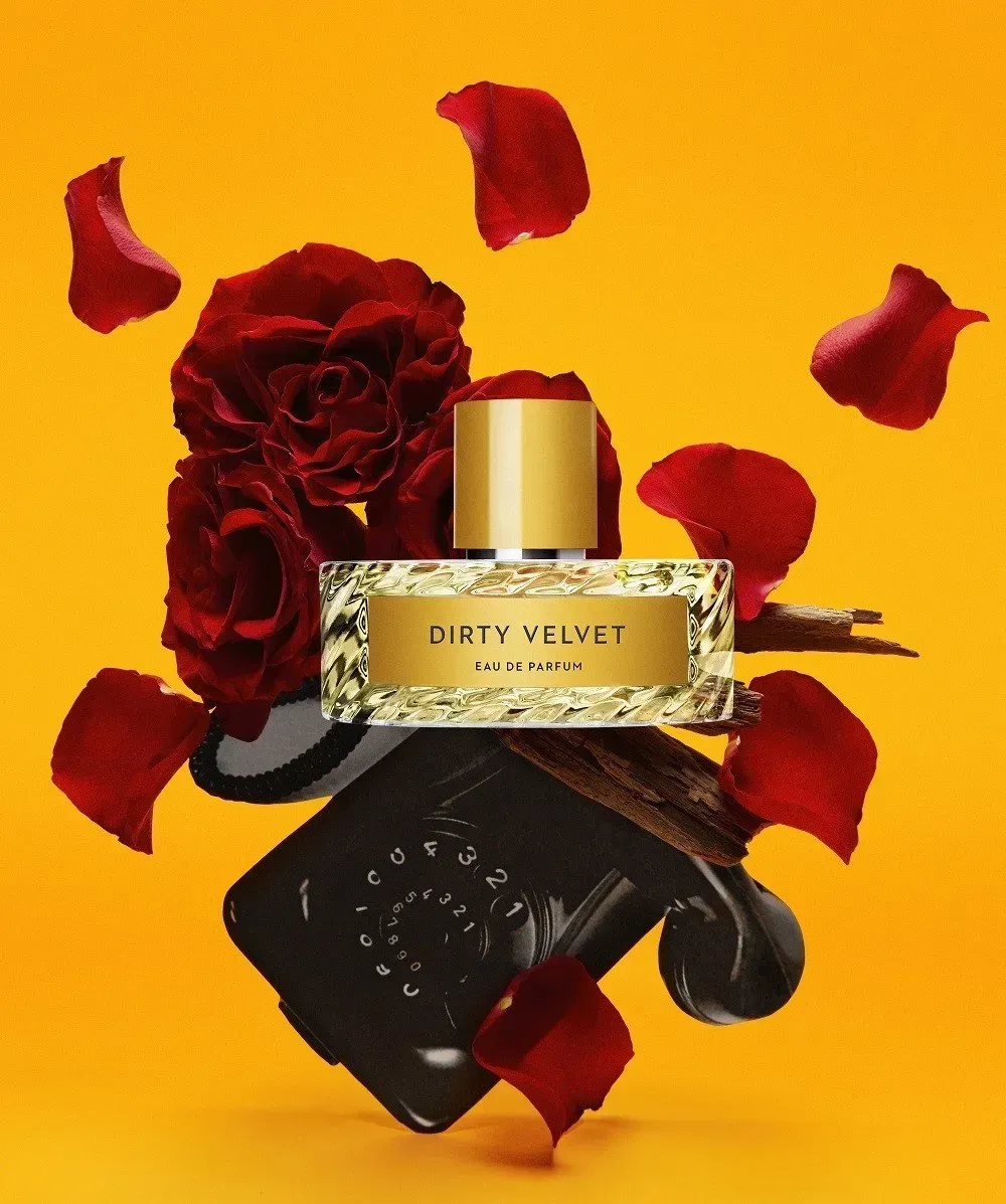Flacone di profumo dorato con rose e petali rossi su sfondo nero con sfondo giallo